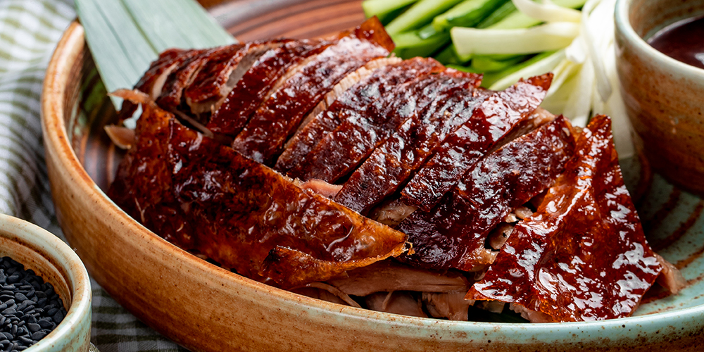 side view of traditional asian food peking duck with cucumbers and sauce on a plate